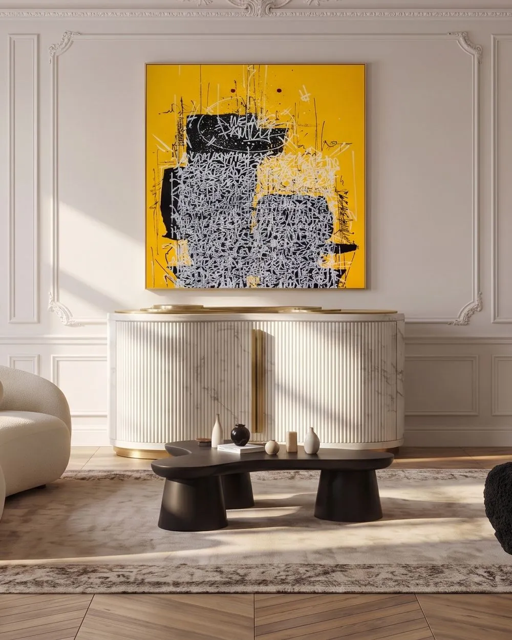 A contemporary living room with white ornate wall moldings, a large yellow and black abstract painting, a white curved sofa with neutral pillows, and a black armchair. A striped marble-top console table with small decorative objects stands against the wall.